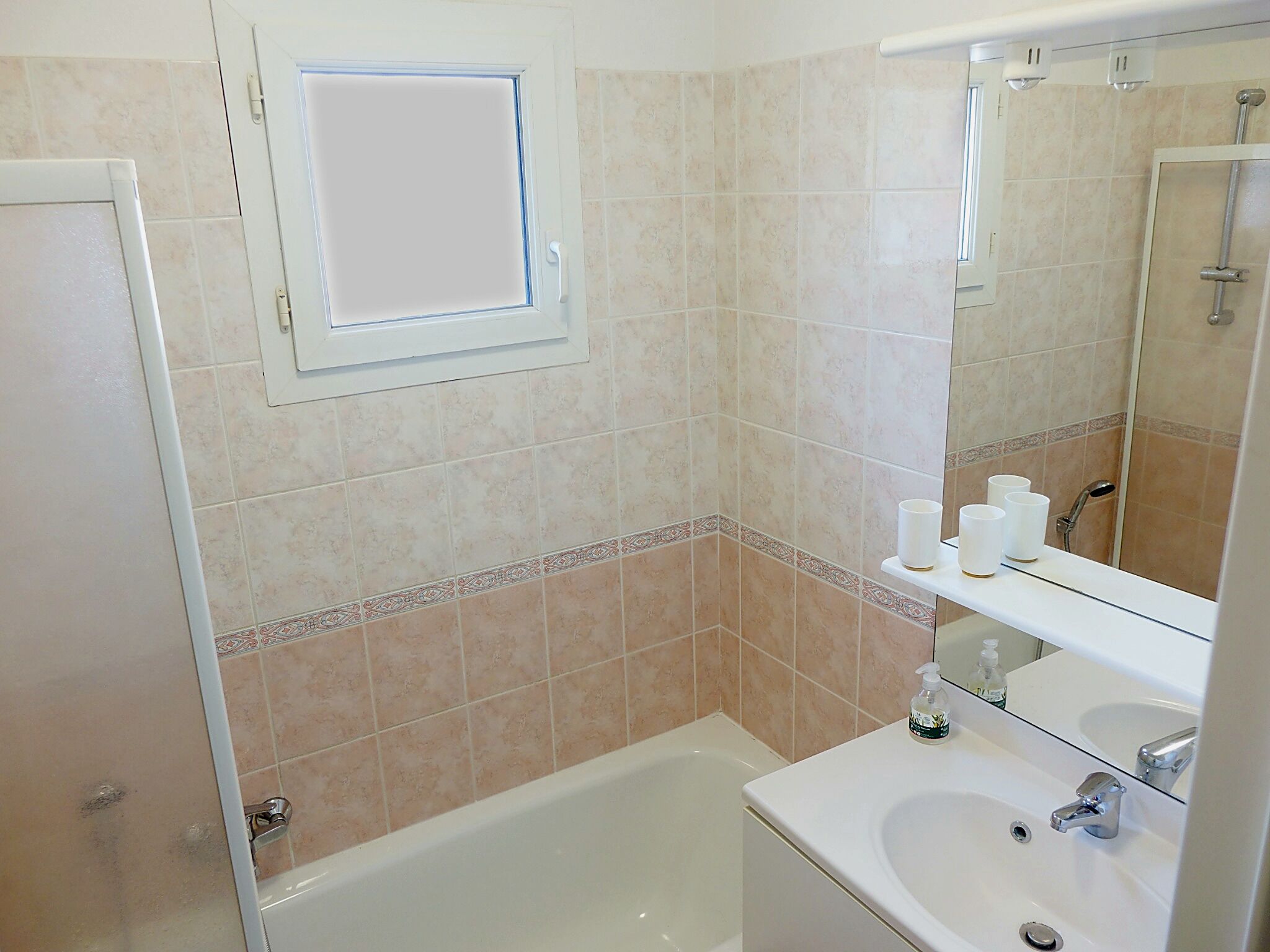 A bathroom with a bathtub, a sink, a mirror, and a shelf with toiletries.