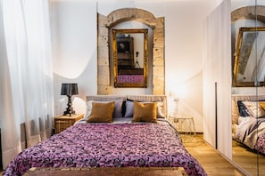 A bedroom with a bed, a lamp, a mirror, and a camera on a tripod.