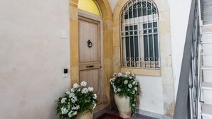 A building entrance with a wooden door, a window with metal bars, and two large flower pots. - Dolce Suite Near Syracuse Cathedral by Wonderful Italy (Syracuse)