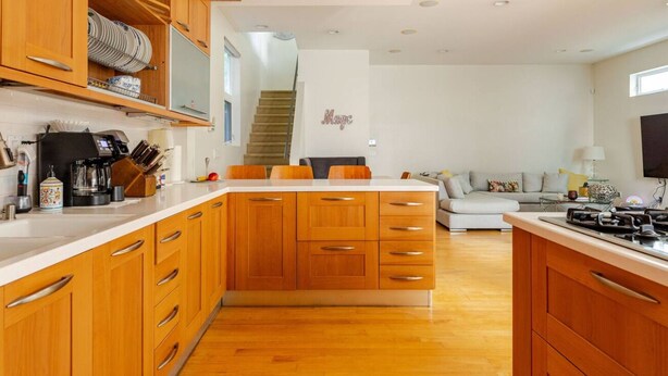 A modern kitchen with wooden cabinets, a central island, and a dining area with a sofa.