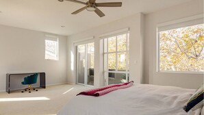 A bedroom with a large bed, a ceiling fan, a desk with a chair, and a sliding glass door leading to a balcony.