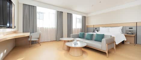 A modern hotel room with a sofa, two round tables, a desk, and a bed with a headboard.