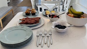 A dining area with a breakfast spread including bacon, muffins, toast, and fruit. - 30A Cottage, Walk to Beach, 2 Pools, Bikes&Chairs (Santa Rosa Beach)