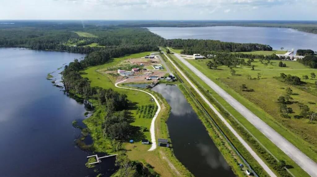 An aerial view of a lakeside property with a road, buildings, and a dock.