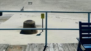 Vista a la playa desde una terraza de madera, con un banco y un letrero.