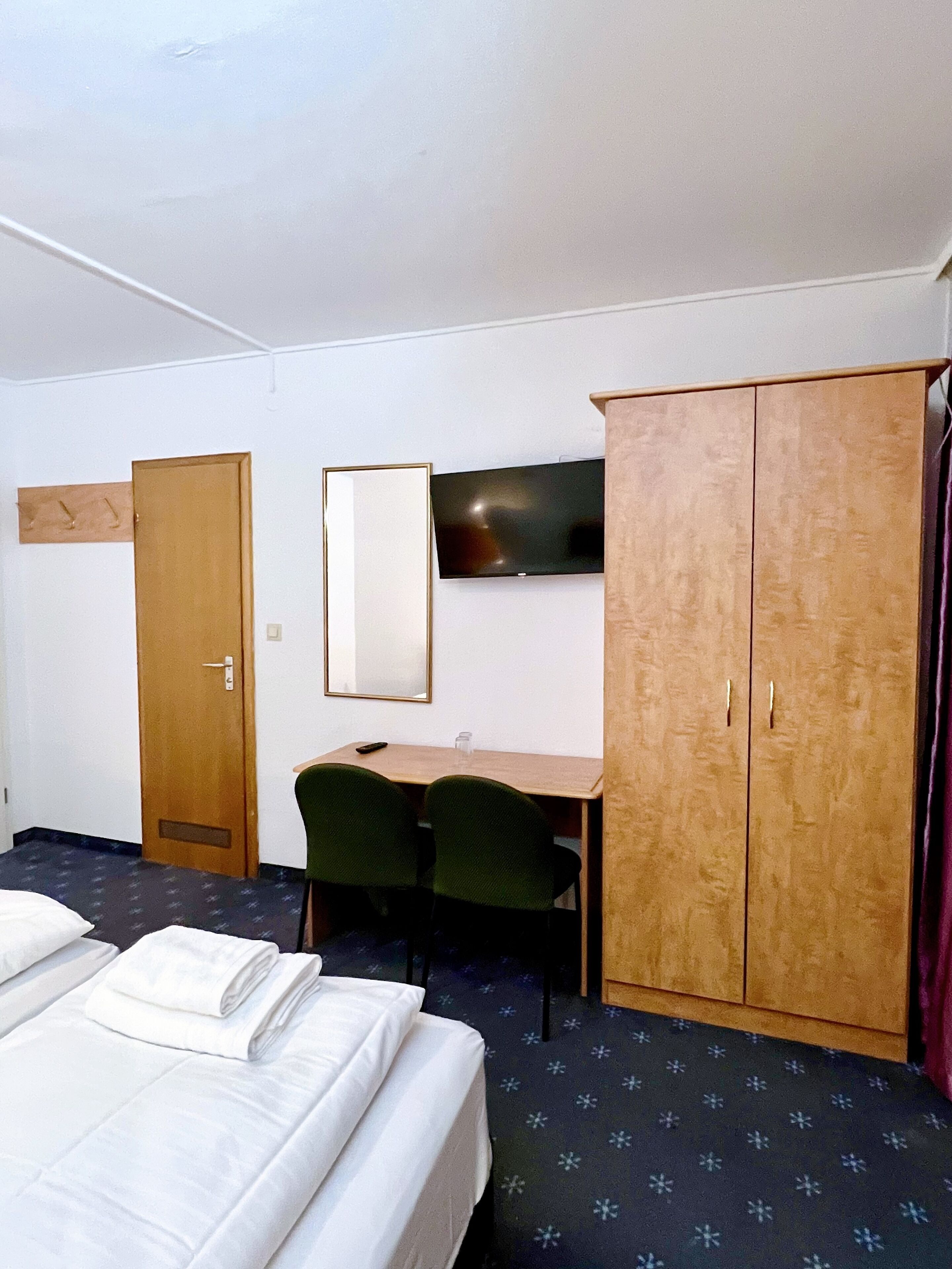 A hotel room with a bed, a desk, a chair, a wardrobe, and a TV on the wall.