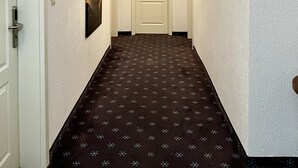 Ein schmaler Flur mit gemustertem Teppich, weißen Wänden und einer Tür am Ende.