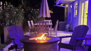 An outdoor seating area with a fire pit, wooden chairs, and an umbrella. - The Capri House: Fun, Grill & Beach Minutes Away (Palm Beach Gardens)
