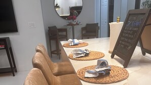 A long dining table with woven placemats and brown leather chairs. A chalkboard sign with a welcome message is visible. - The Capri House: Fun, Grill & Beach Minutes Away (Palm Beach Gardens)