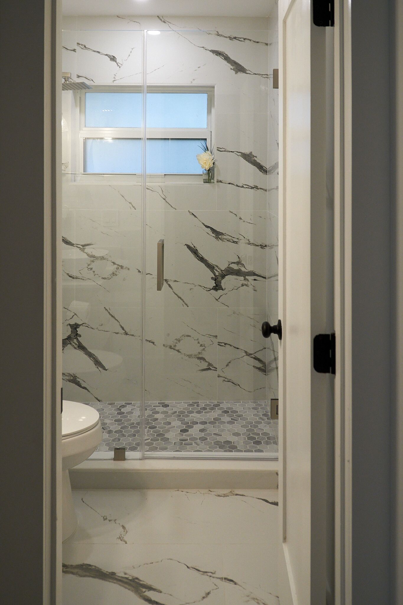 Un baño con ducha envuelta en vidrio, inodoro y ventana.