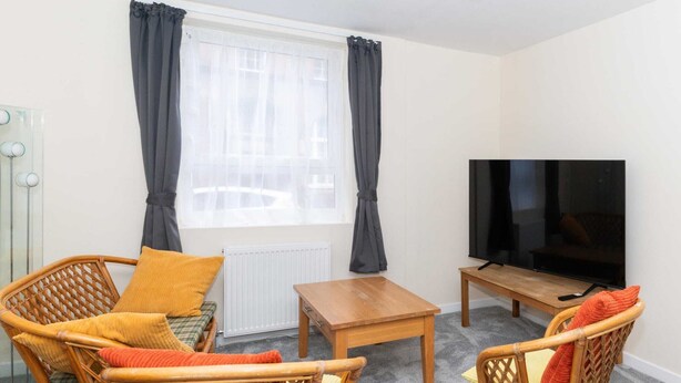 Ein möbliertes Wohnzimmer mit Rattanmöbeln, einem Fernseher und einem fenster mit Vorhängen.