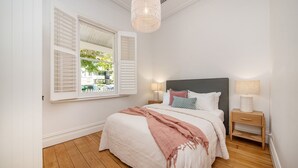 Et soveværelse med seng, natborde, et vindue med skodder og en hængende lampe.