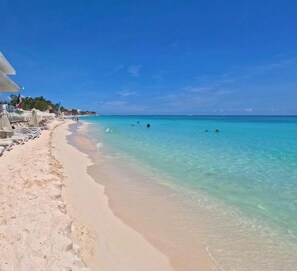 Una playa con agua turquesa cristalina, arena dorada y sombrillas.