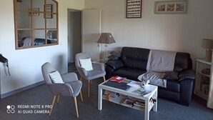 Un salón con un sofá de cuero negro, dos sillones grises, una mesa de centro blanca con revistas y una lámpara.