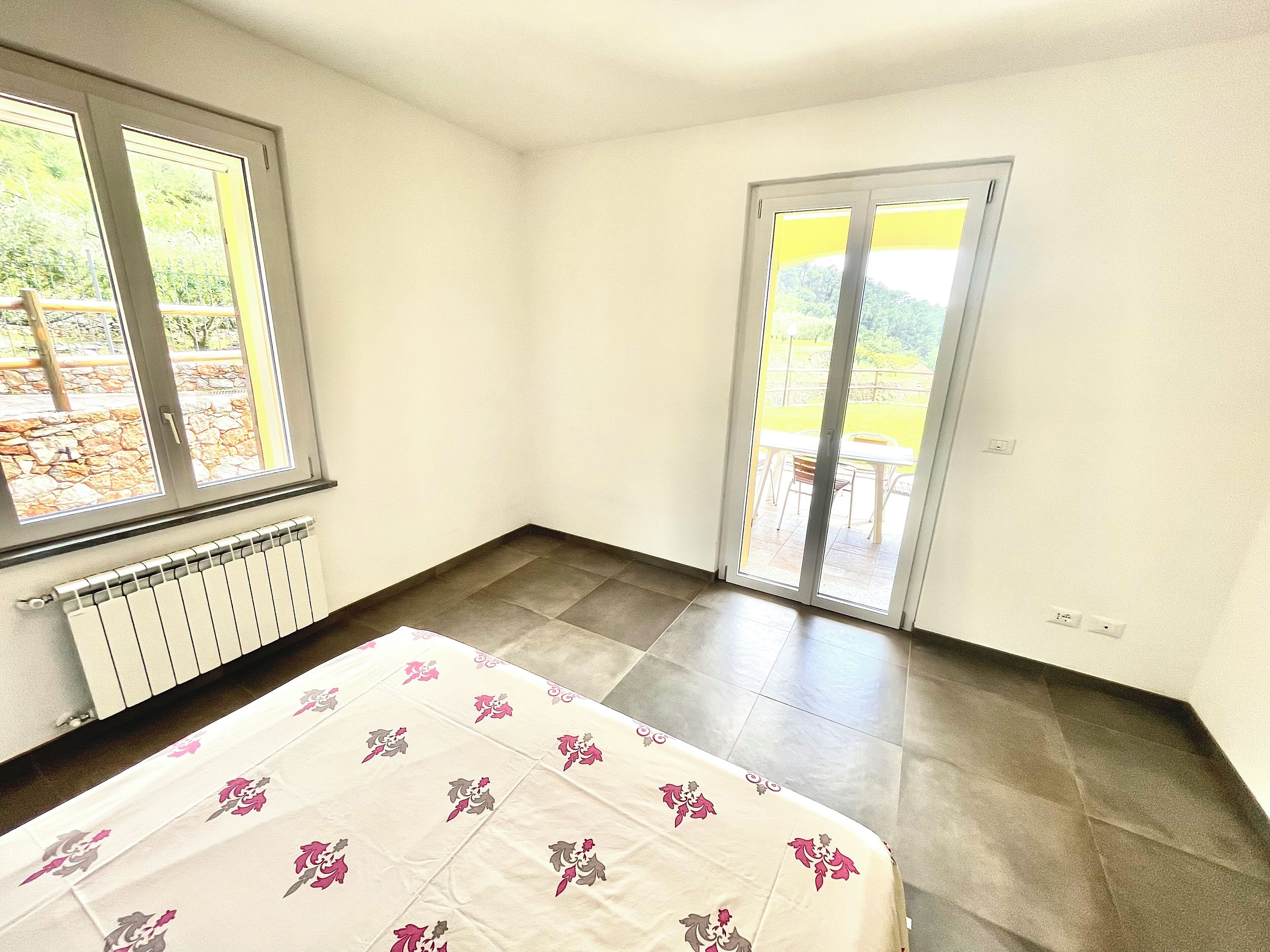 A bedroom with a bed, a radiator, a window, and a sliding glass door leading to an outdoor area.