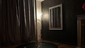 A room with a circular floor lamp, a mirror on the wall, and a curtain partially drawn. - Gîte Coquin (Augan)