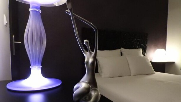 A modern hotel room with a bed, a nightstand, a lamp, and a decorative sculpture. - Gîte Coquin (Augan)