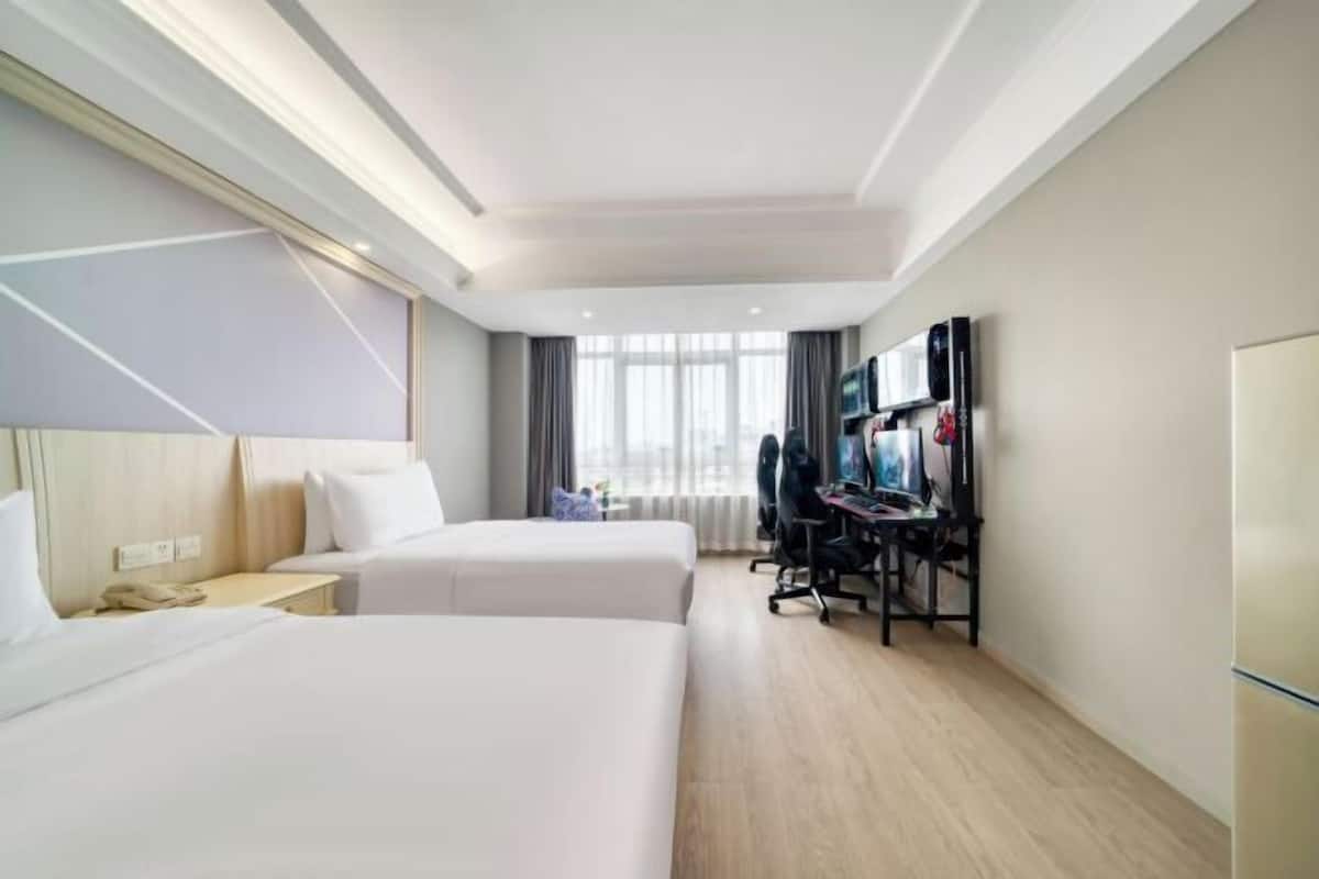 Habitación de hotel con dos camas, un escritorio con computadora, un televisor y una ventana con cortinas.
