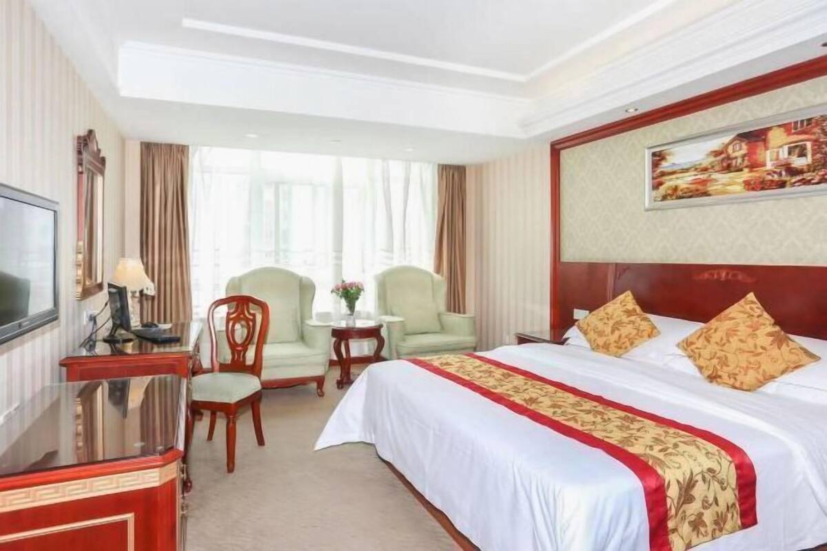 Habitación de hotel con cama, escritorio, dos sillones, televisor y un cuadro en la pared.