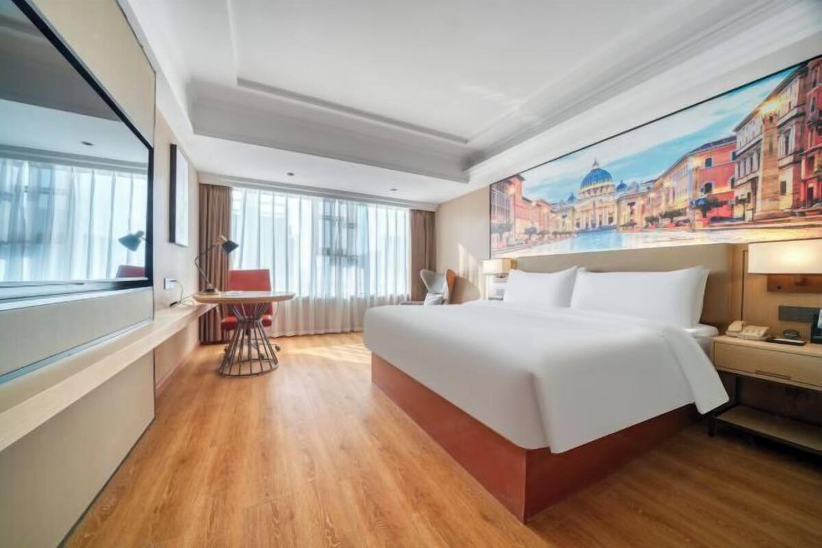 Habitación de hotel con una cama grande, un escritorio, una silla, una ventana con cortinas y un cuadro en la pared.