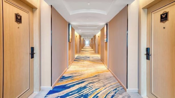 Um corredor de hotel com piso de mármore, portas de madeira e teto com iluminação embutida.