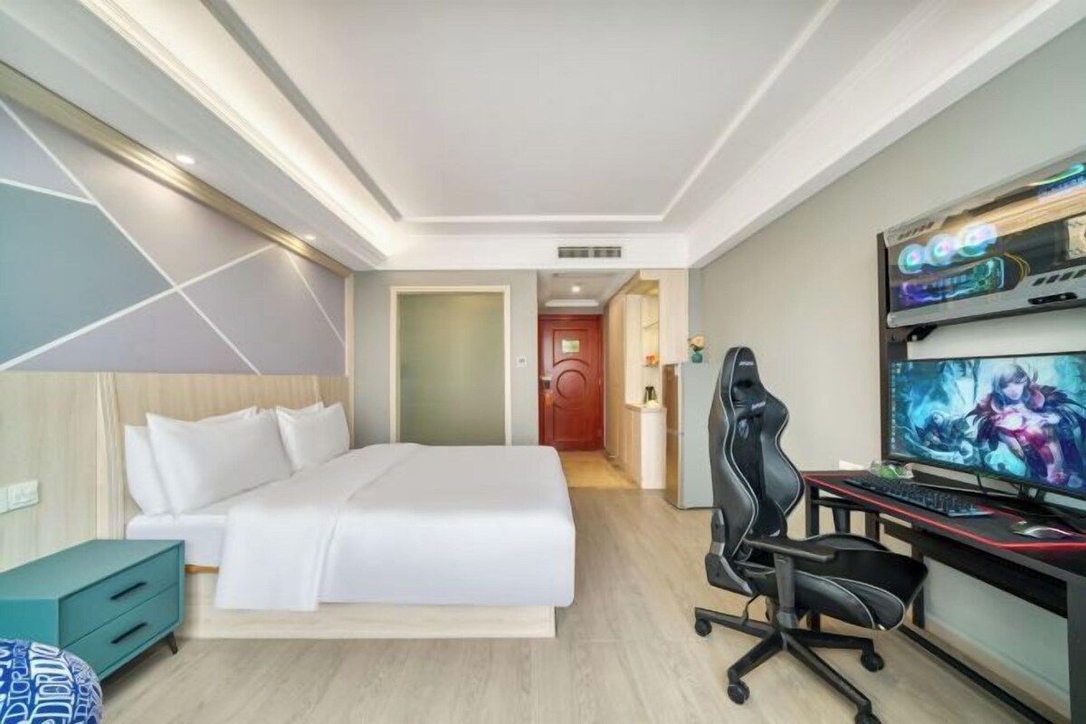 A hotel room with a bed, desk, computer, and TV.