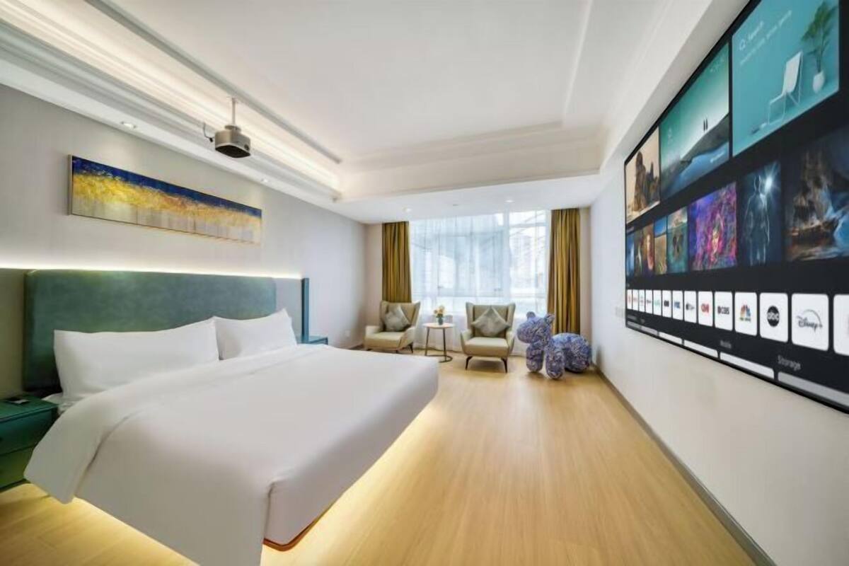 Habitación de hotel con una cama grande, un escritorio, dos sillas, una mesita y una pared con cuadros.