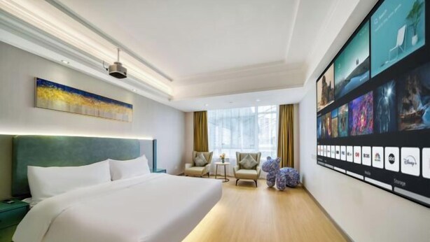 A hotel room with a large bed, a seating area with chairs, a small table, and a wall-mounted TV displaying various channels. - Vienna Hotel Ningbo Jiangbei Avenue Wanda Branch (Ningbo)