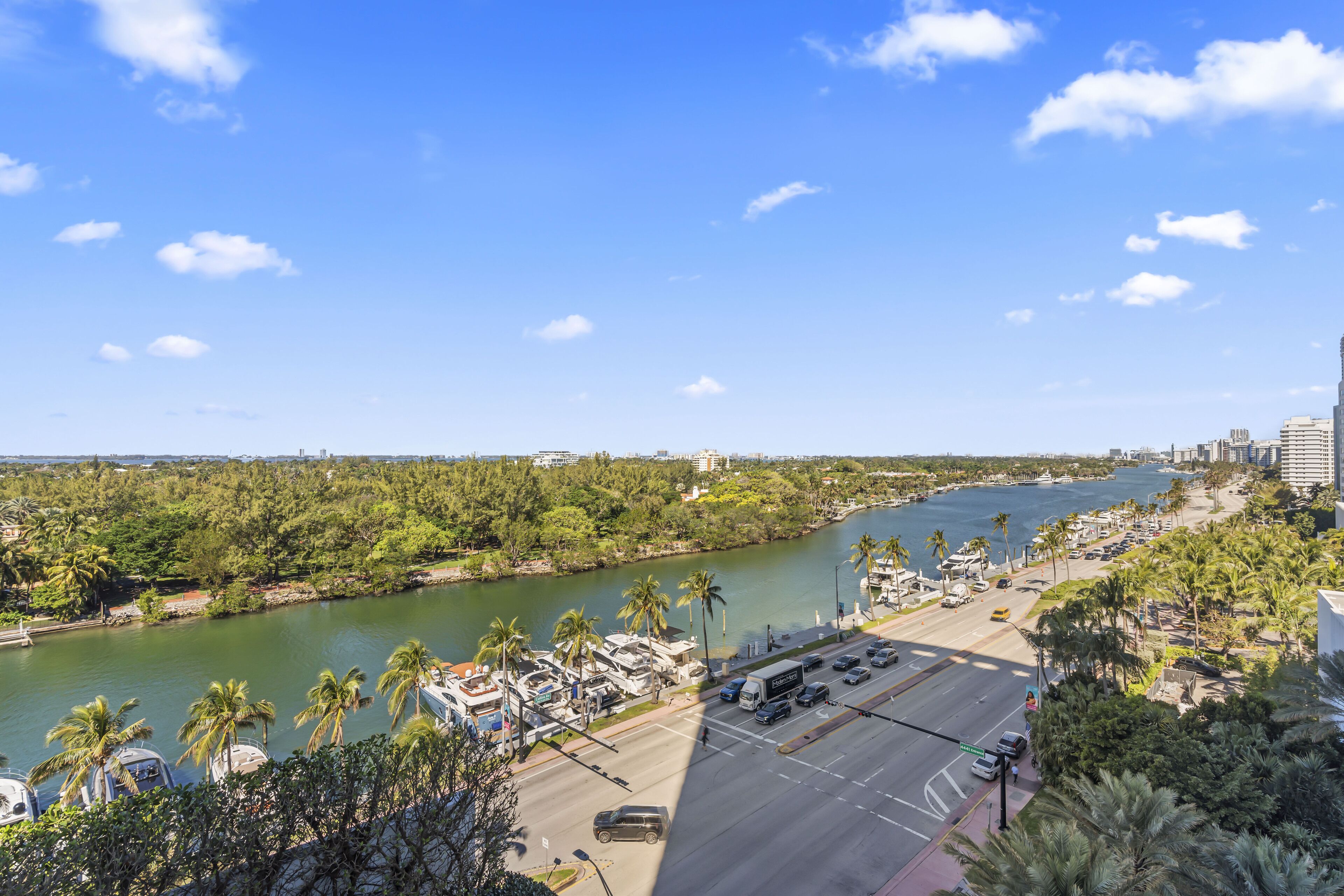 A riverside view with a road, parked vehicles, and a marina.