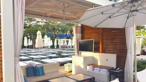 A sunlit outdoor lounge area with seating, a flat-screen TV, and umbrellas. - Fontain Miami Beach - Bayview Condo - We Host (Miami Beach)