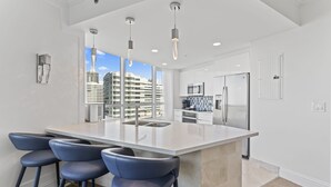 A modern kitchen with a large island, bar stools, stainless steel appliances, and a view of a cityscape. - Fontain Miami Beach - Bayview Condo - We Host (Miami Beach)