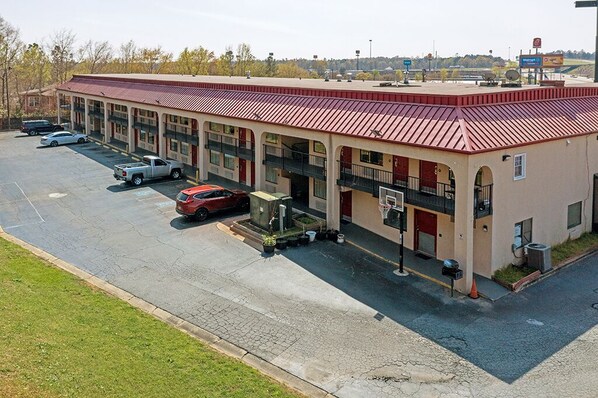 A motel with a red roof and multiple balconies, a parking lot with several cars, and a Walmart sign in the background. - REGENCY INN & SUITES (Macon)