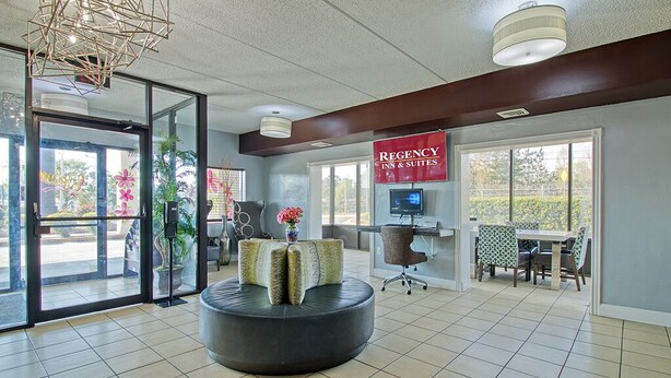 A lobby with a reception desk, a seating area with a round table and chairs, and a sign for 'REGENCY INN & SUITES'. - REGENCY INN & SUITES (Macon)