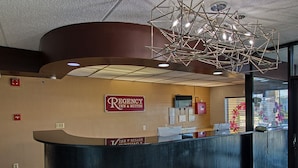 A reception area with a curved counter, a modern chandelier, and a sign for Regency Inn & Suites. - REGENCY INN & SUITES (Macon)