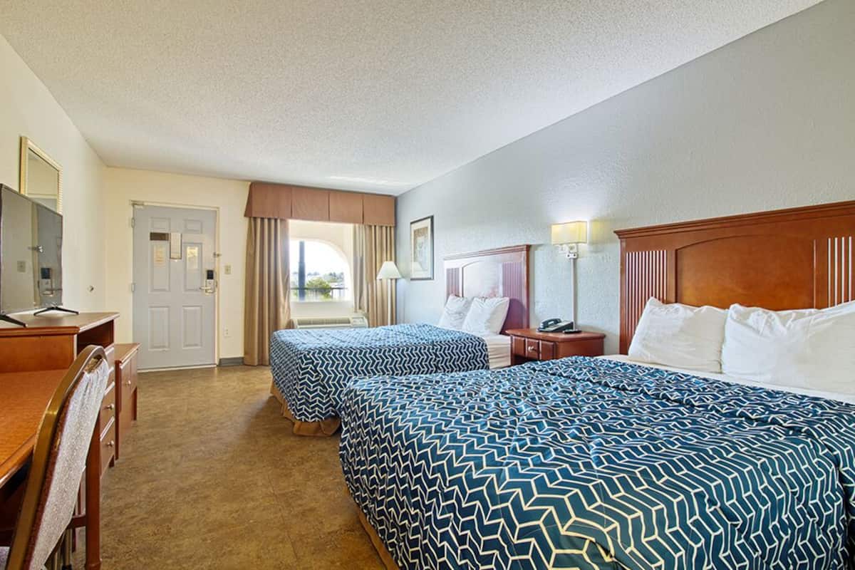 A hotel room with two beds, a desk, a chair, a TV, and a door leading to a balcony.