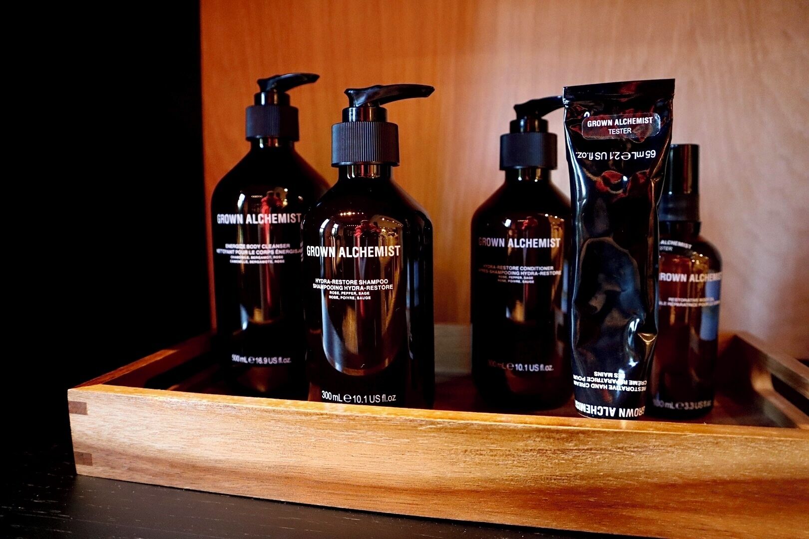 A wooden tray holding various bottles of 'Grown Alchemist' skincare products.