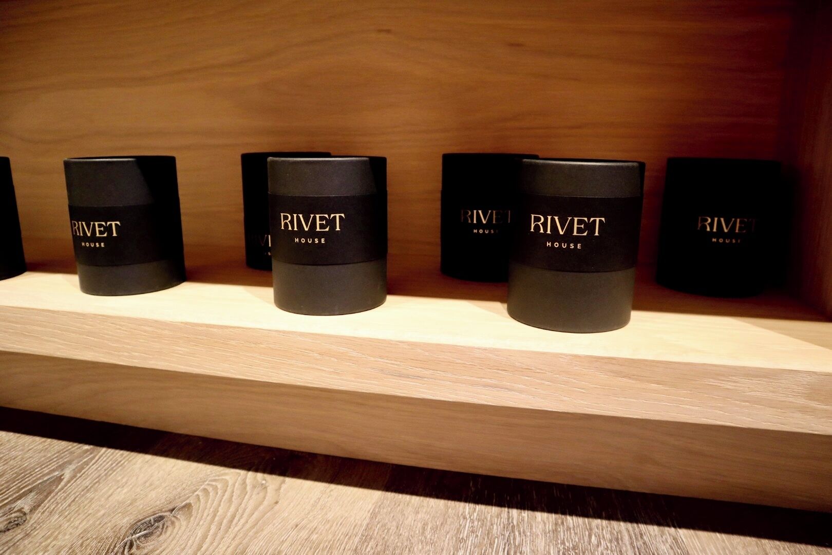 A wooden shelf displaying four black cylindrical containers labeled "Rivet House".