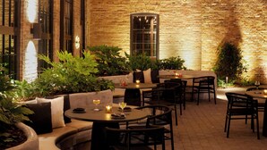 An outdoor dining area with brick walls, string lights, and potted plants. - Rivet House (Athens)