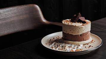 Un postre en capas sobre un plato con migas y trozos de chocolate sobre una mesa de madera oscura.