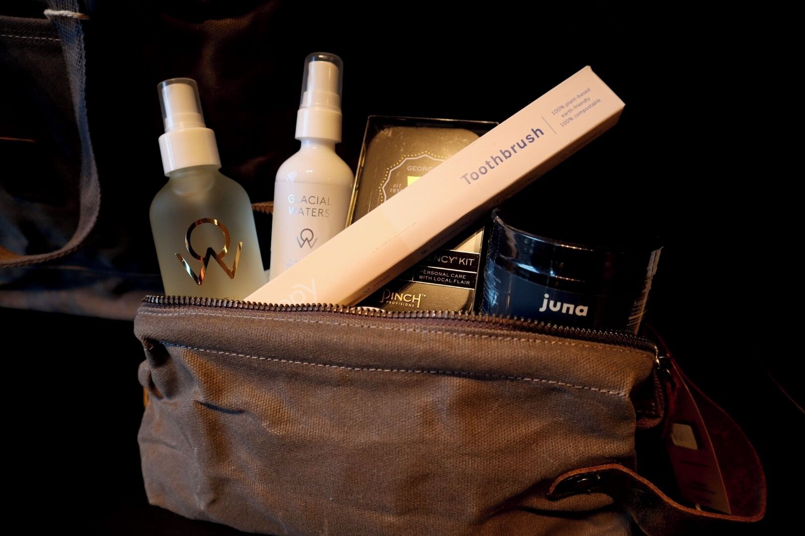 Una borsa da viaggio con uno spazzolino, una bottiglia di tonico viso, una confezione di prodotto per la cura della pelle e una scatola di articoli per l'igiene personale.