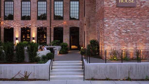 A brick building with a sign reading "Rivet House." There are steps leading to the entrance, and string lights are visible. - Rivet House (Athens)
