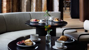 A cozy dining area with two round tables, each with plates of pastries, cups, and a vase with flowers. - Rivet House (Athens)