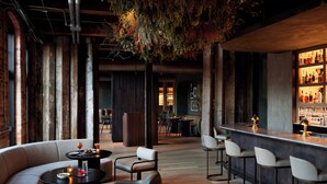 A bar area with a long counter, bar stools, and a seating area with sofas and a round table. - Rivet House (Athens)