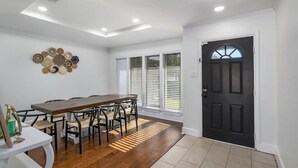 A dining area with a wooden table and chairs, a decorative wall piece, and a black door. - Lone Star house  by AT&T, Six Flags ,Globe life,Pool-Jacuzzi! (Grand Prairie)