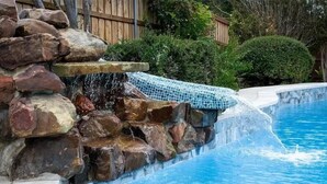A swimming pool with a rock waterfall feature and a blue mosaic border. - Lone Star house  by AT&T, Six Flags ,Globe life,Pool-Jacuzzi! (Grand Prairie)
