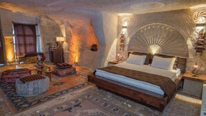 A cozy bedroom with a large bed, a wooden nightstand, a wall-mounted lamp, and a decorative fan. - Theodora Village  (Ürgüp)
