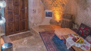 A rustic stone interior with a wooden door, a small window, and a stone bench. - Theodora Village  (Ürgüp)