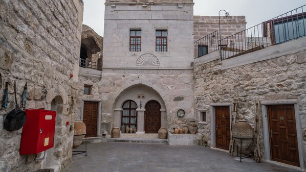 A courtyard with stone buildings, wooden doors, and a red electrical box.