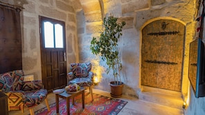 A cozy room with a wooden door, a potted plant, a colorful patterned sofa, and a small table with fruits. - Theodora Village (Ürgüp)