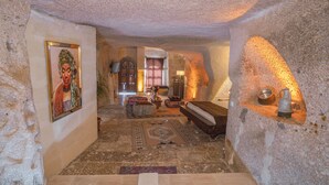 A stone-walled interior with a wooden bench, a table with a vase, and a framed picture on the wall. - Theodora Village  (Ürgüp)
